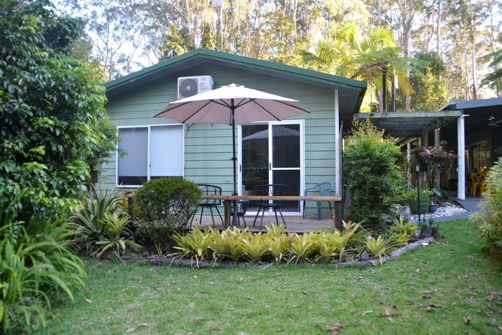 A small house with a deck, outdoor furniture, and a large umbrella.