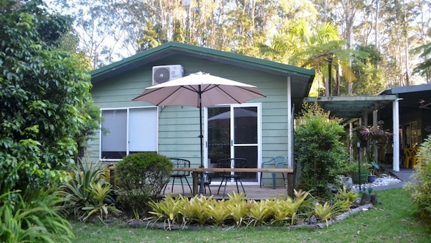 Ein kleines Haus mit einer Terrasse, Gartenmöbeln und einem großen Sonnenschirm.