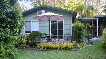 A small house with a deck, outdoor furniture, and a large umbrella.