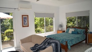 Ein Schlafzimmer mit Bett, Sofa, Deckenventilator und Fenster mit Blick auf Grünflächen.