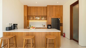 A modern kitchen with wooden cabinets, a white countertop, and a built-in black refrigerator. - Villa Omah Bumbak (Badung)