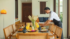A dining table set with breakfast items, a vase of flowers, and a lit candle. - Villa Omah Bumbak (Badung)