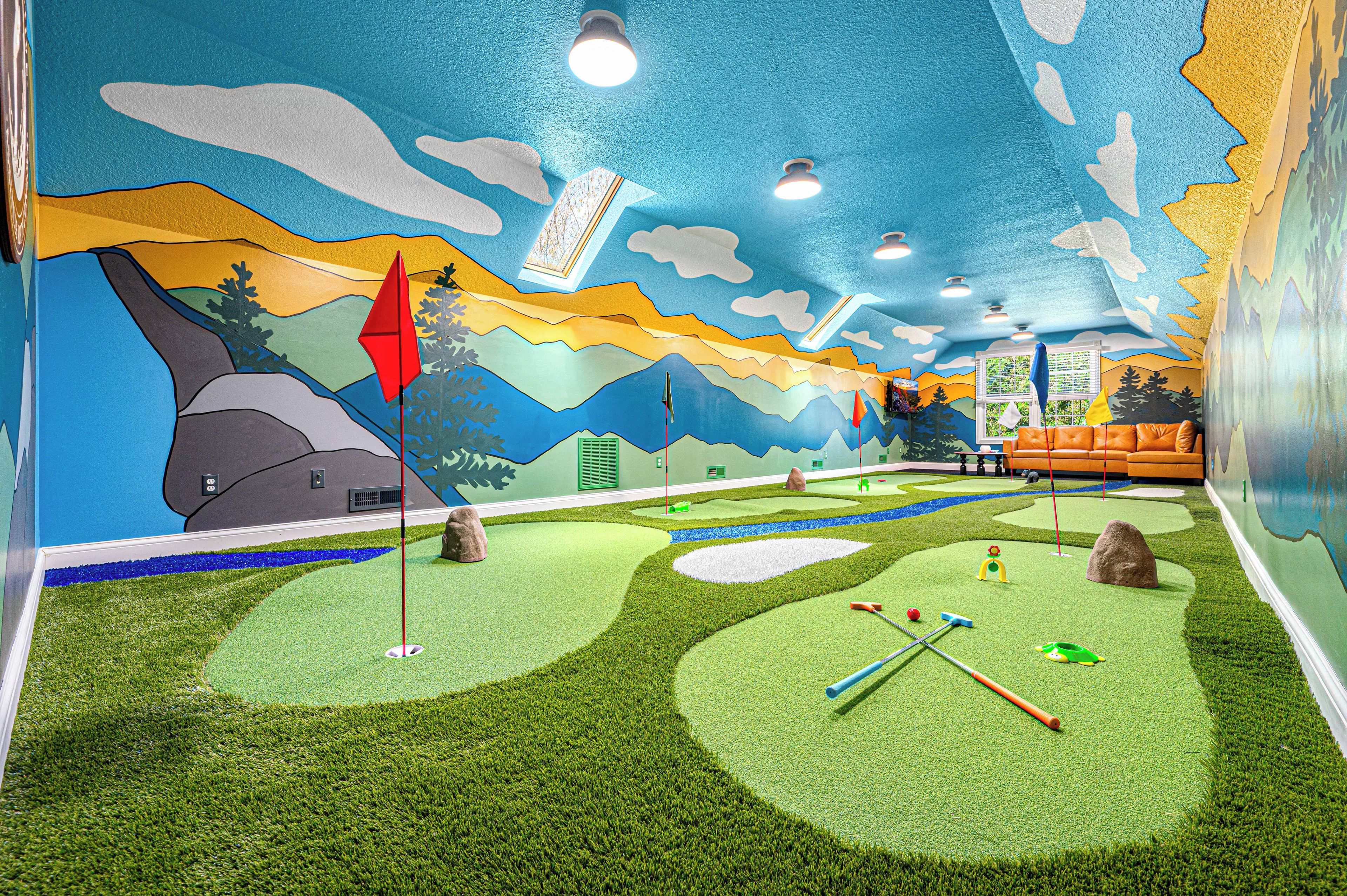 A room with a mural of a landscape, a golf putting area, and a seating area with a couch.