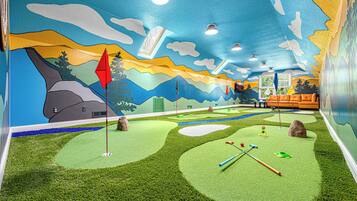 A room with a mural of a landscape, a golf putting area, and a seating area with a couch.