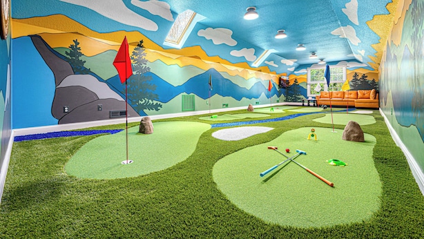 Quarto com mural de paisagem, espaço para jogar golfe e área de estar com sofá.