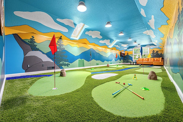Une pièce décorée d’une fresque représentant un paysage, avec un espace dédié à l’entraînement au golf et un coin salon doté d’un canapé.