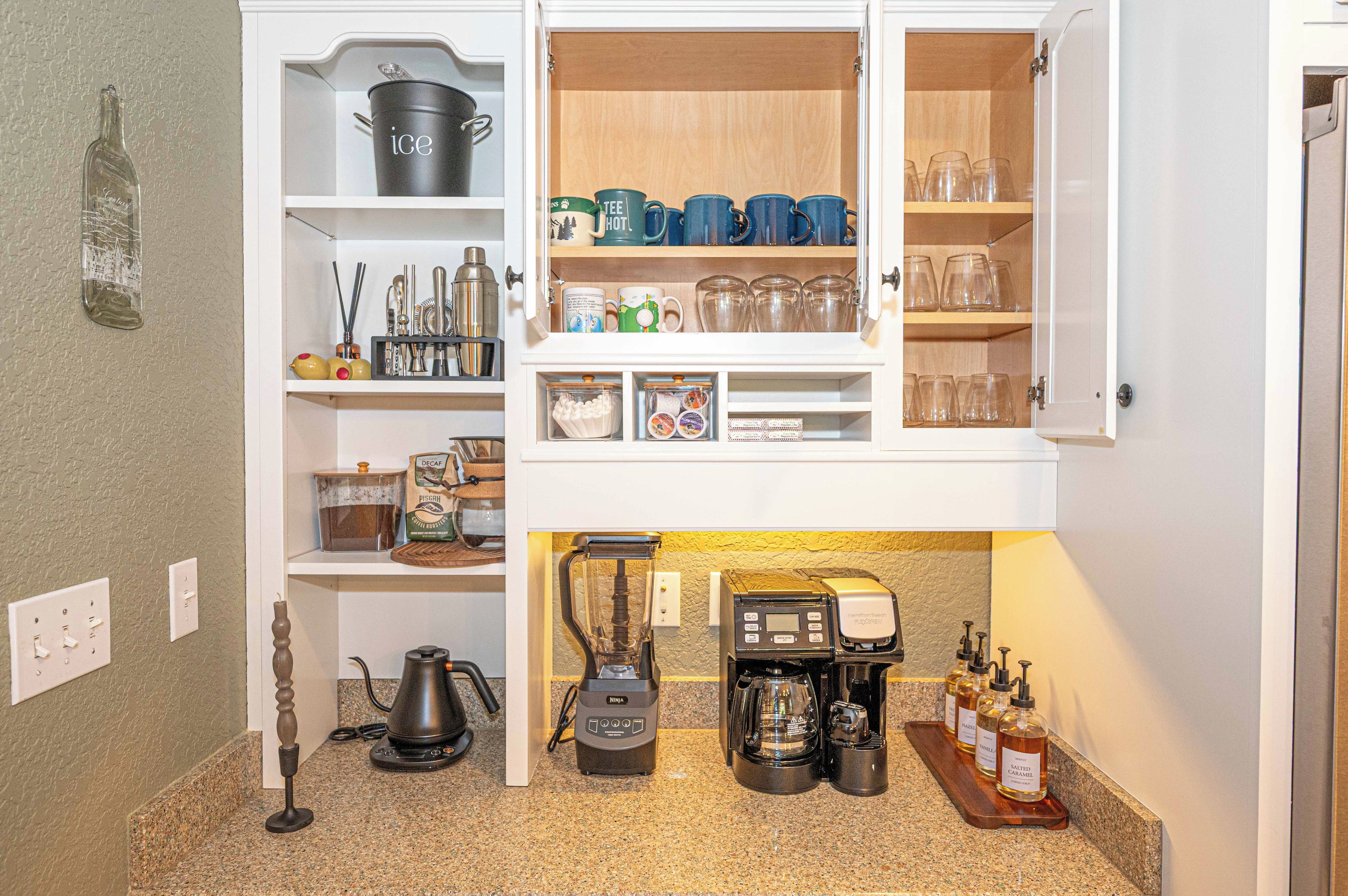 Une cuisine équipée d’un espace dédié à la préparation du café, comprenant une machine à café, un moulin et un espace de rangement pour les grains de café.
