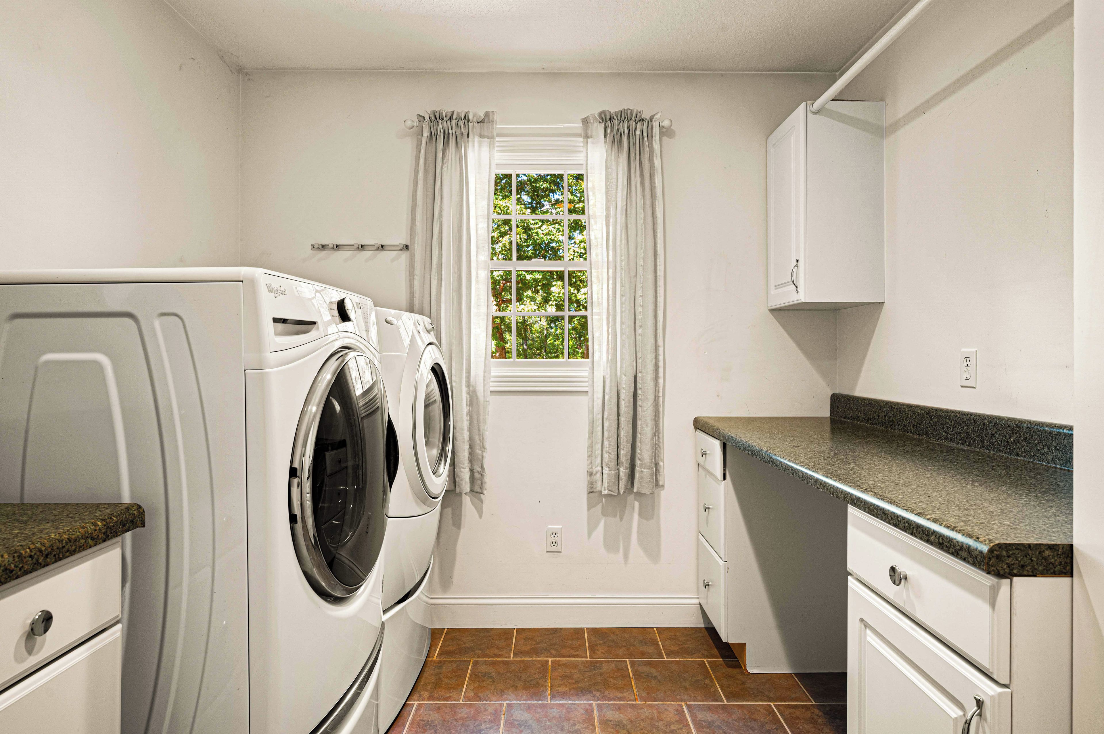 Une petite buanderie équipée d’un lave-linge et d’un sèche-linge à chargement frontal, d’une fenêtre avec des rideaux et d’un plan de travail.