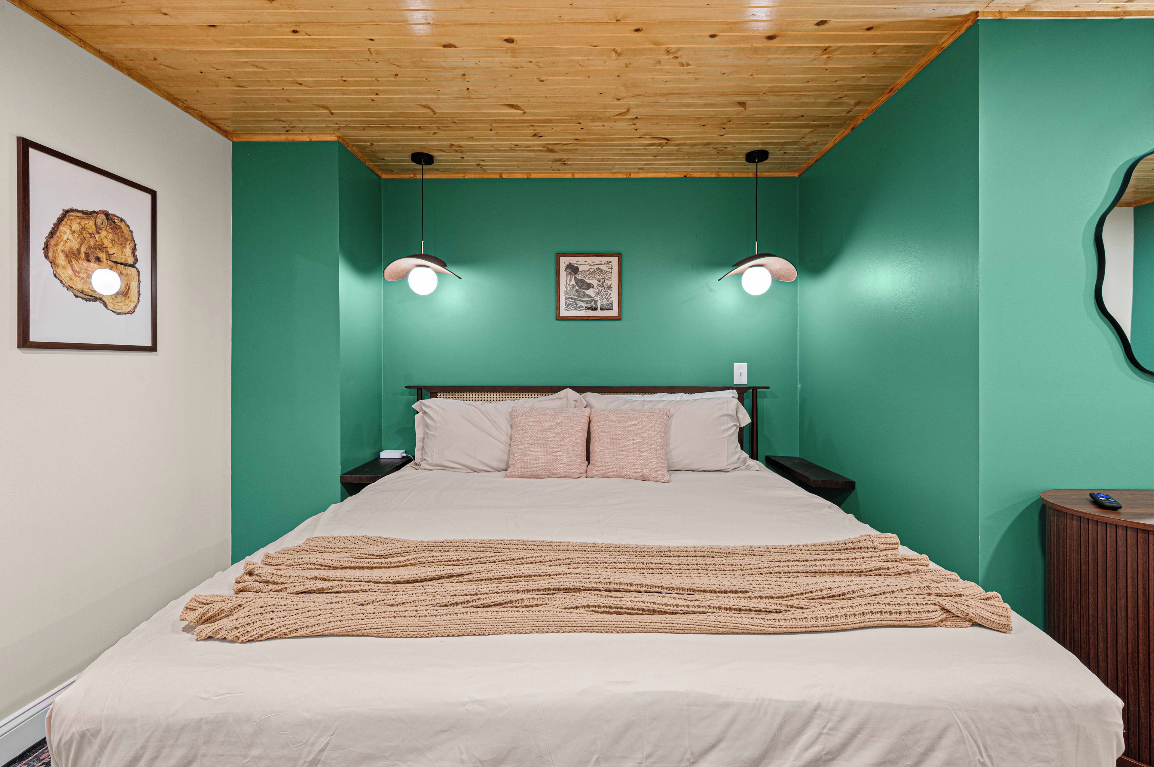 Une chambre à coucher avec un lit, un plafond en bois, des murs verts, deux lampes fixées au mur et un tableau encadré.