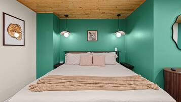 Une chambre à coucher avec un lit, un plafond en bois, des murs verts, deux lampes fixées au mur et un tableau encadré.
