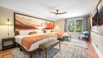 A bedroom with a large bed, two bedside tables, a bench, a ceiling fan, a window with curtains, and a painting on the wall.