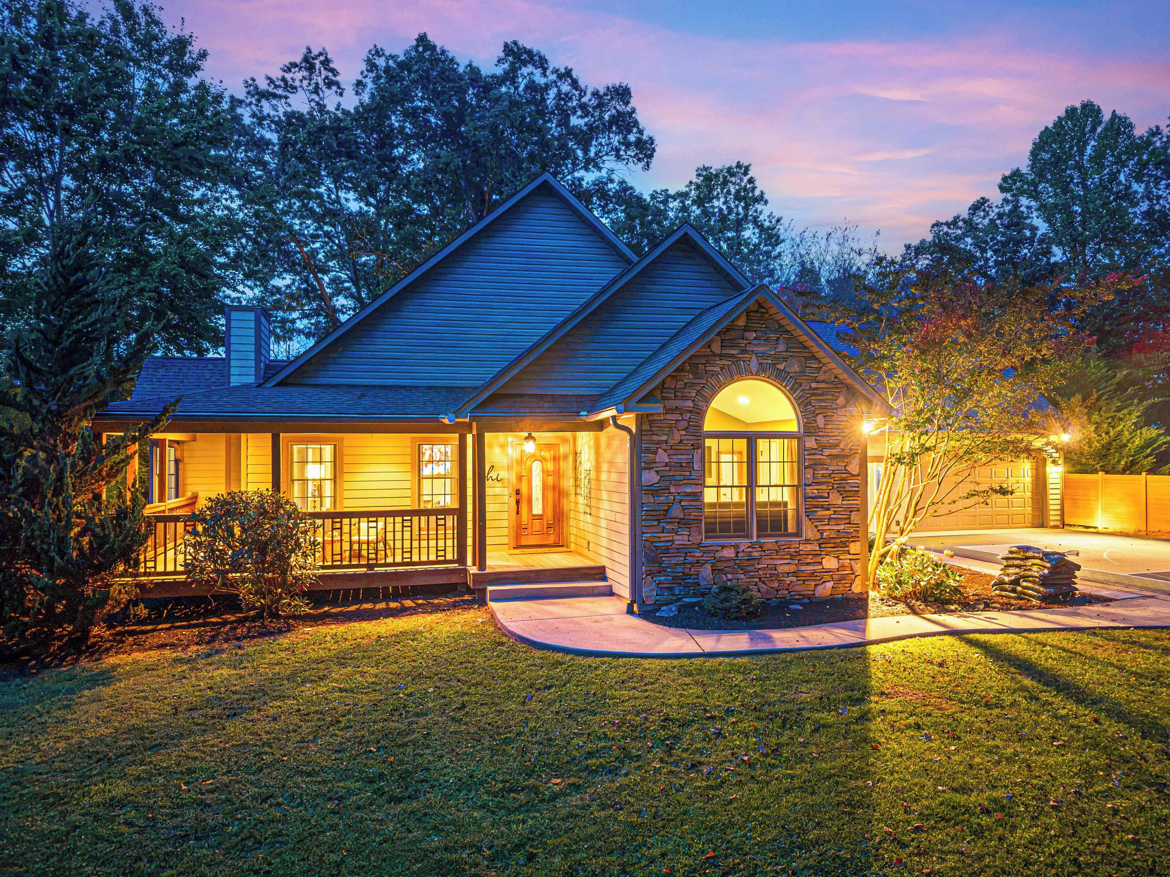 A two-story house with a stone archway entrance, a covered porch, and a well-lit front yard.