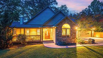 A two-story house with a stone archway entrance, a covered porch, and a well-lit front yard.