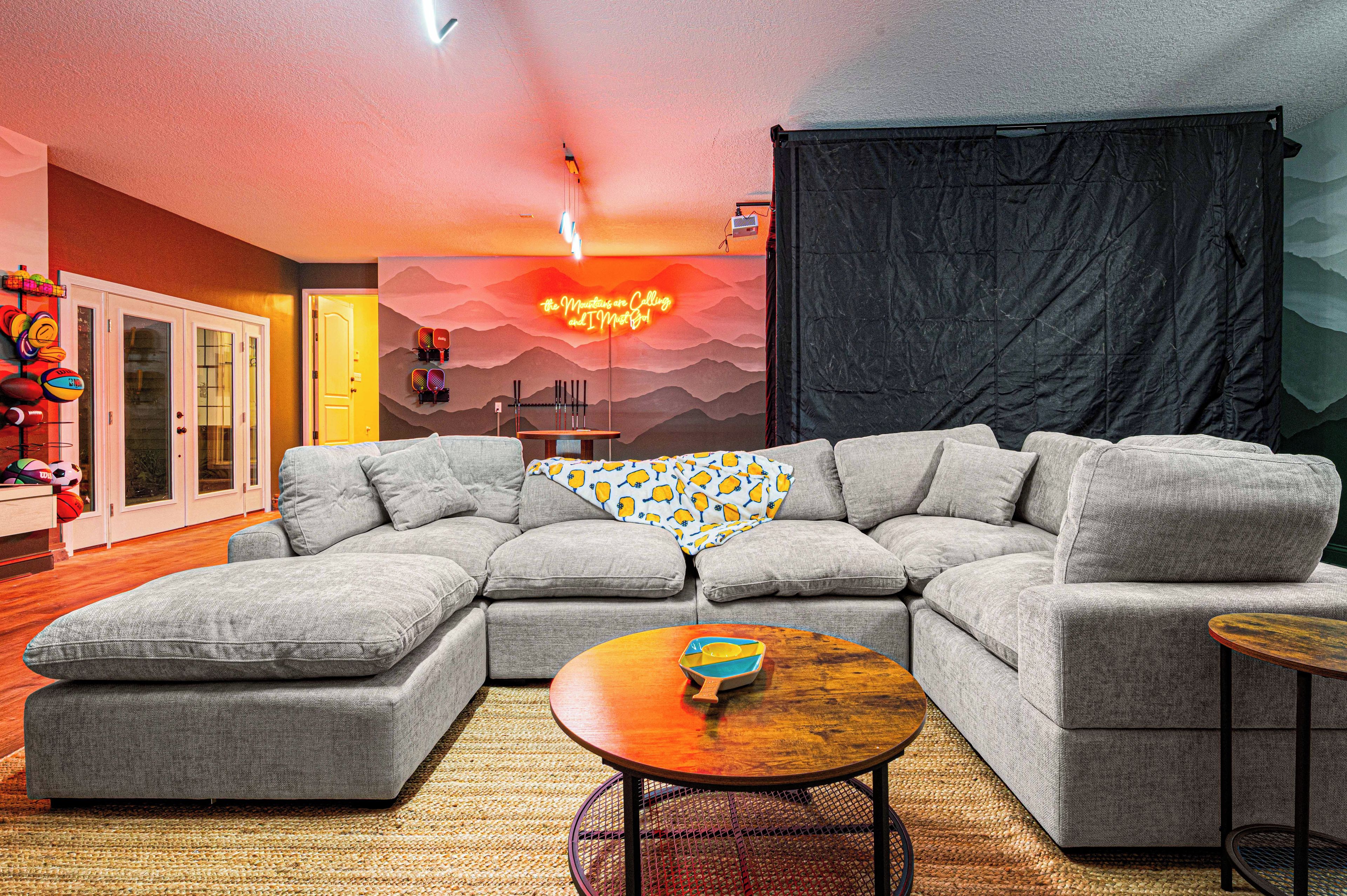 A modern living room with a sectional sofa, a coffee table, and a wall with a neon sign.