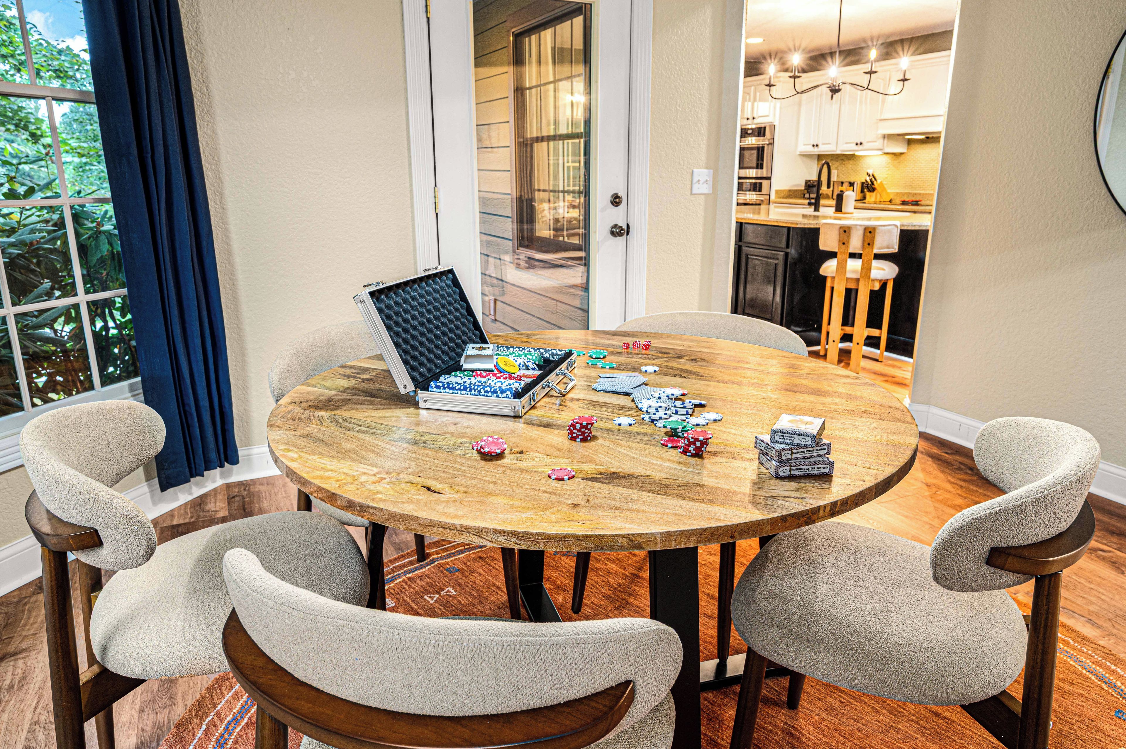 A round wooden table with poker chips and cards, surrounded by four upholstered chairs.