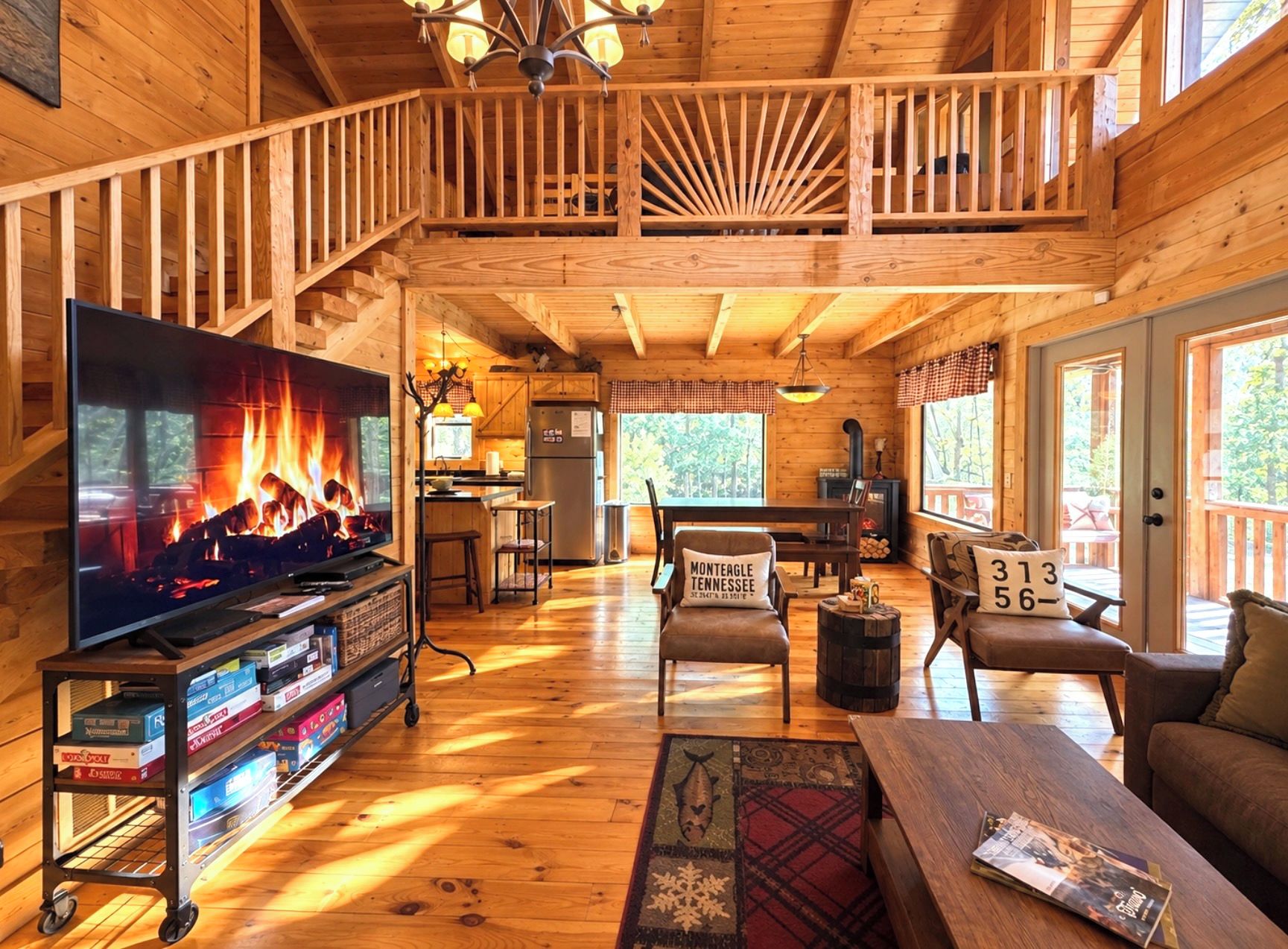 Interior de una cabaña amplia de madera con televisor grande, chimenea, comedor y balcón.
