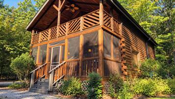 Une cabane en rondins dotée d’un balcon, d’un escalier et offrant une vue sur la forêt environnante.