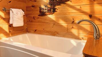Interior de una cabaña de madera con una bañera, paredes de madera, un perchero para toallas y un adorno metálico.