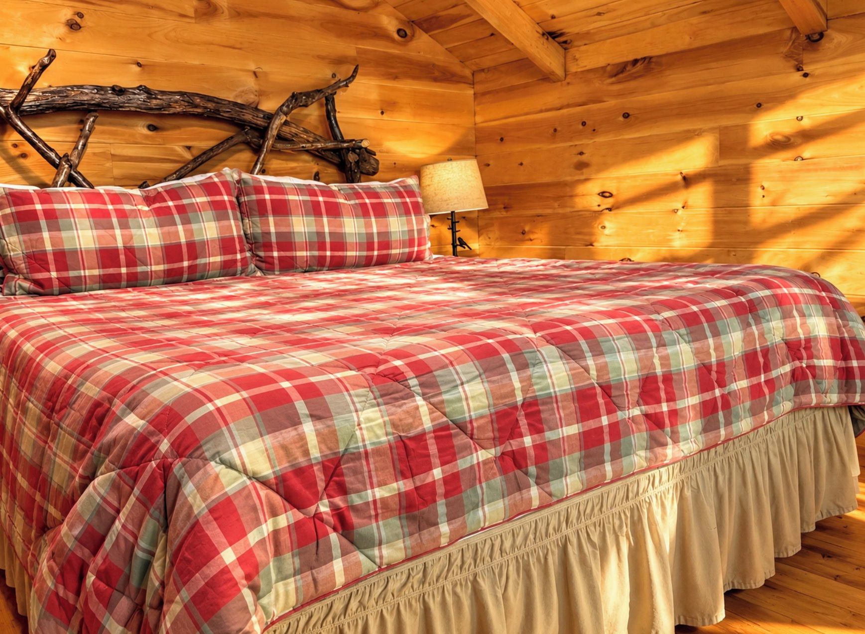 A bed with a plaid bedspread and matching pillows in a wooden room with a rustic ceiling.