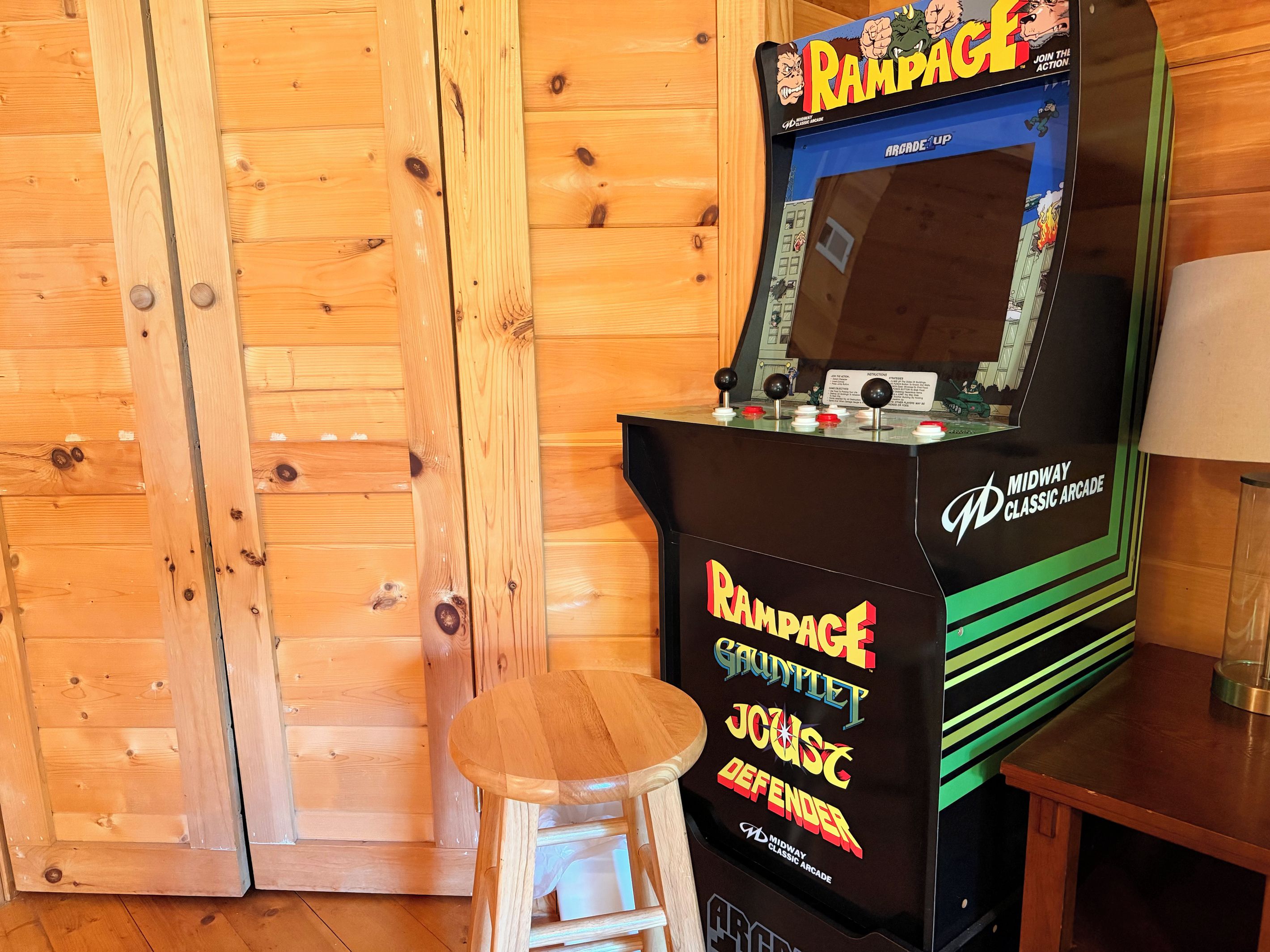 Una máquina de videojuegos clásica con un joystick y botones, ubicada junto a un taburete de madera.