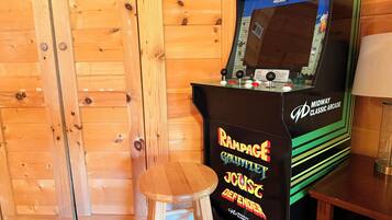 Una máquina de videojuegos clásica con un joystick y botones, ubicada junto a un taburete de madera.