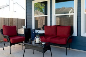 A patio with two red cushioned chairs, a black wicker table, and a candle holder. - Luxury 3BR/3.5BA Sanctuary Near Downtown -Garage - EV Charger -Generator (Houston)