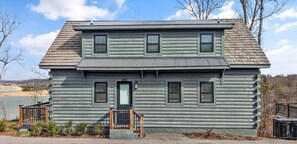 A two-story log cabin with a front porch, a number '1367' on the door, and a view of a lake in the background. - Smoky Mtn Game Haven Overlooking Douglas Lake 3-Bdrm Cabin w/Hot Tub Sevierville (Sevierville)