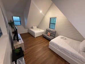 A small, triangular attic bedroom with a white bed, a grey sofa, and a white chair. There are two windows with blinds, and a small plant on a shelf. - Smoky Mtn Game Haven Overlooking Douglas Lake 3-Bdrm Cabin w/Hot Tub Sevierville (Sevierville)