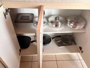 A kitchen cabinet with three shelves, containing cookware and pots.