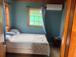 Ein Schlafzimmer mit einem Bett, einem Fenster mit Vorhängen, einer Klimaanlage und einer Holztür.