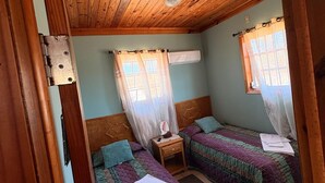 A room with two beds, a wooden ceiling, and a window with a curtain. - perfect for family. Angler and nature guides (Owens Town)