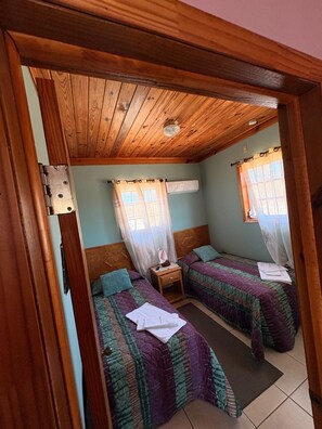 Ein Zimmer mit zwei Betten, einer Holzbalkendecke und einem Fenster mit Vorhang.
