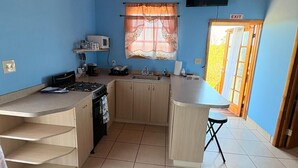A compact kitchen with a stove, sink, and cabinets, a window with curtains, and a door marked 'EXIT'. - perfect for family. Angler and nature guides (Owens Town)