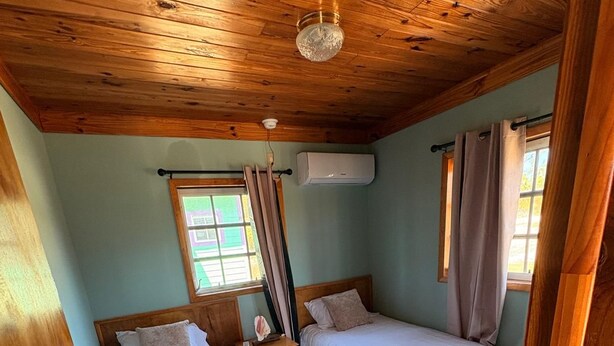A room with two beds, a wooden ceiling, a window with curtains, and an air conditioning unit. - perfect for family. Angler and nature guides (Owens Town)