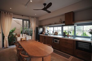 A modern kitchen with a wooden table, built-in appliances, and a large window. - Serene Tropical Stay with Pool Near Hoi An Old Town (Đà Nẵng)