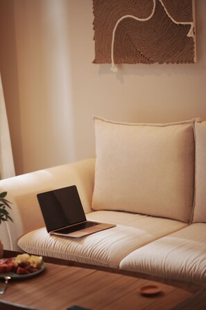 Un ordinateur portable posé sur un canapé beige, avec une tapisserie murale tissée au-dessus.