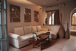 A modern living room with a sectional sofa, a wooden coffee table, abstract wall art, and a large window with curtains. - Serene Tropical Stay with Pool Near Hoi An Old Town (Đà Nẵng)