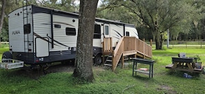 Un veicolo ricreativo (RV) parcheggiato in un'area erbosa con una veranda in legno adiacente.