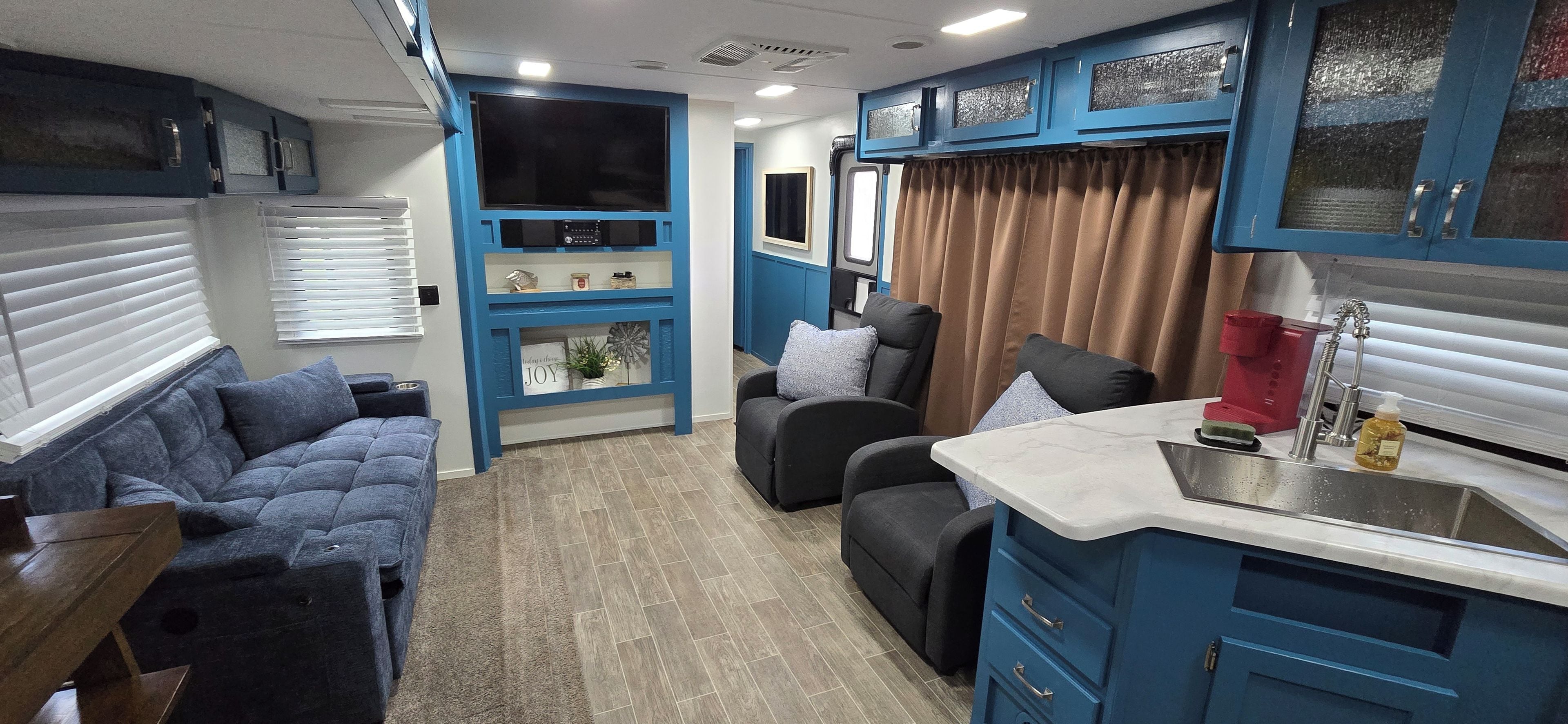 A compact living space with a kitchenette, a sofa, a chair, and a small table.