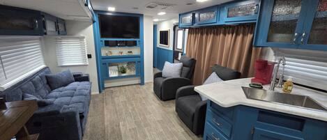 A compact living space with a kitchenette, a sofa, a chair, and a small table.