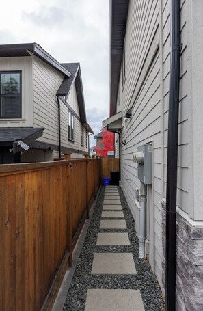 Un étroit passage entre deux bâtiments, avec une clôture en bois d’un côté et un coffret électrique de l’autre.