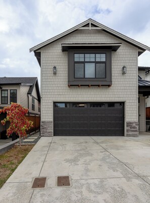 A two-story house with a garage, a window with blinds, and a small tree with red leaves. - The Haven Retreat | 1-Bedroom | Near Victoria (LANGFORD)