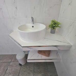A bathroom with a white marble sink, a small potted plant, and a trash bin. - Jungle View Resort (Ko Chang)