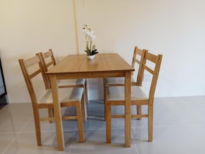 Ein Holztisch mit vier Stühlen, einer kleinen Topfpflanze und einem Fliesenboden.