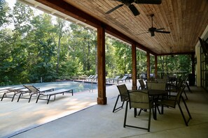 Un espace extérieur abrité, doté d’une piscine, de chaises longues et de tables, le tout entouré d’arbres.