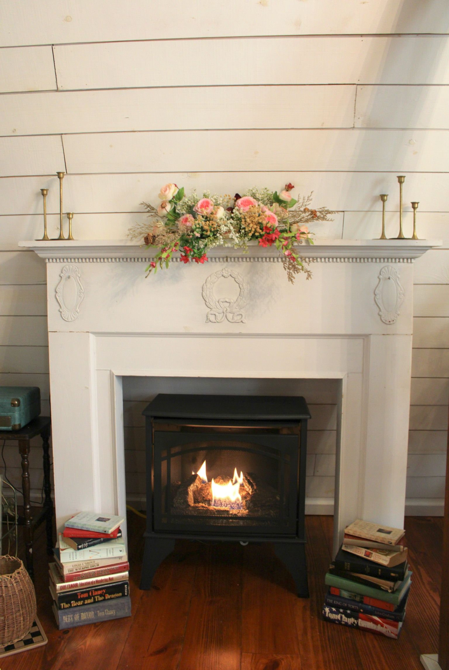 A fireplace with a mantel decorated with flowers and candles, surrounded by books.