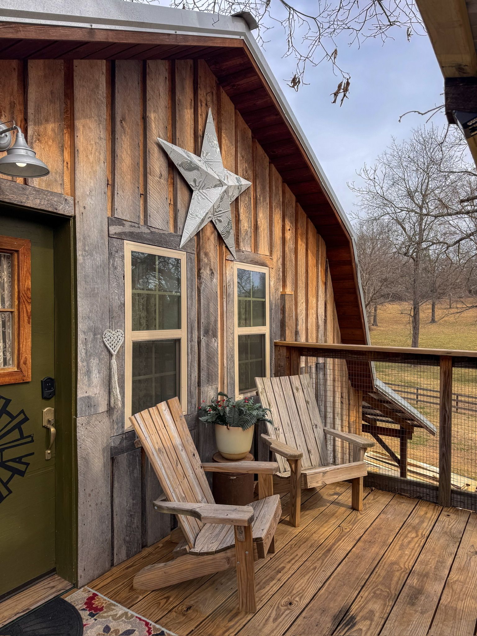 A wooden cabin with a porch, two Adirondack chairs, a star decoration, and a green door.