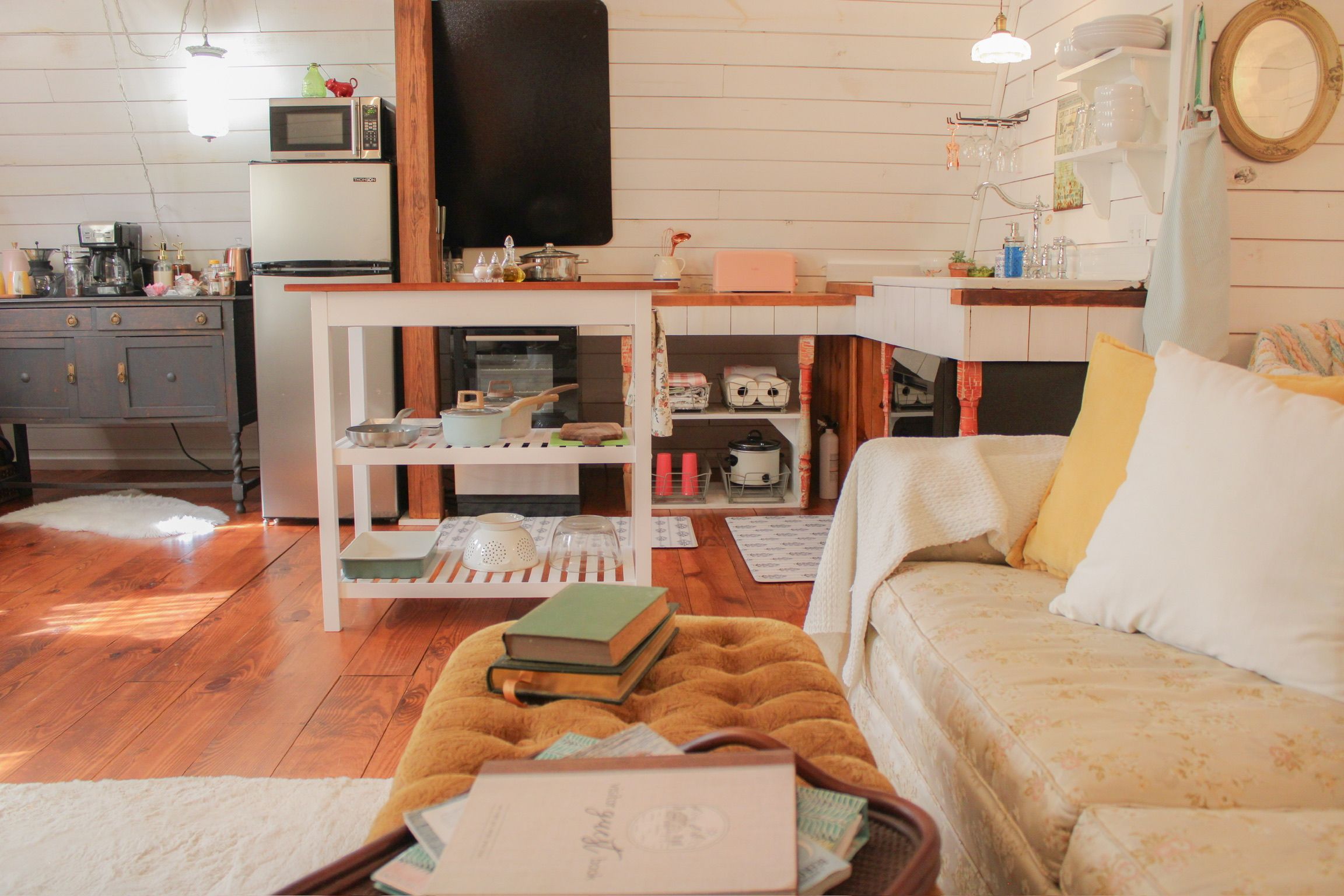 A cozy living room with a sofa, a coffee table with books, a kitchen area with appliances, and a dining table with dishes.