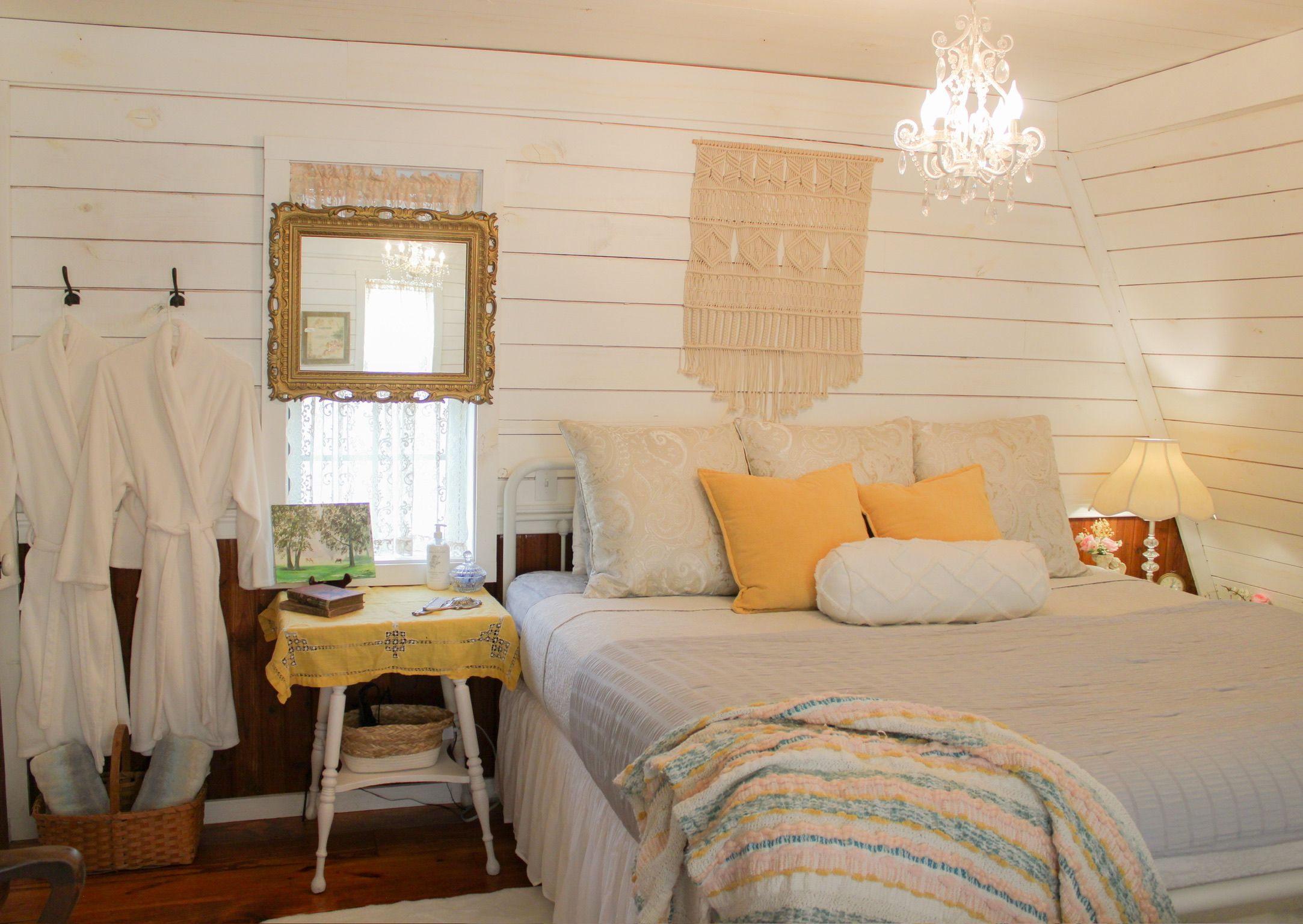 A bedroom with a bed, a bedside table, a mirror, a chandelier, and a window with curtains.