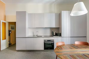 A modern kitchen with white cabinets, a built-in oven, and a dining area with a striped table. - New Flat with Artistic Flair (Milano)